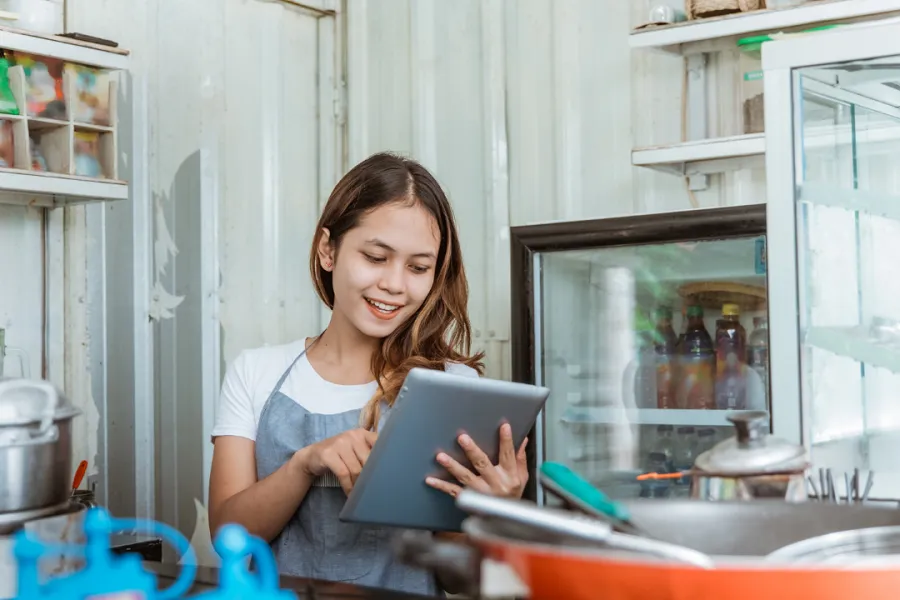 A lady standing in the kitchen and reviewing online ordering on her tablet